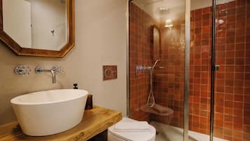 Une salle de bain avec un meuble-lavabo en bois, un lavabo blanc, un miroir et une douche en verre avec des carreaux rouges.