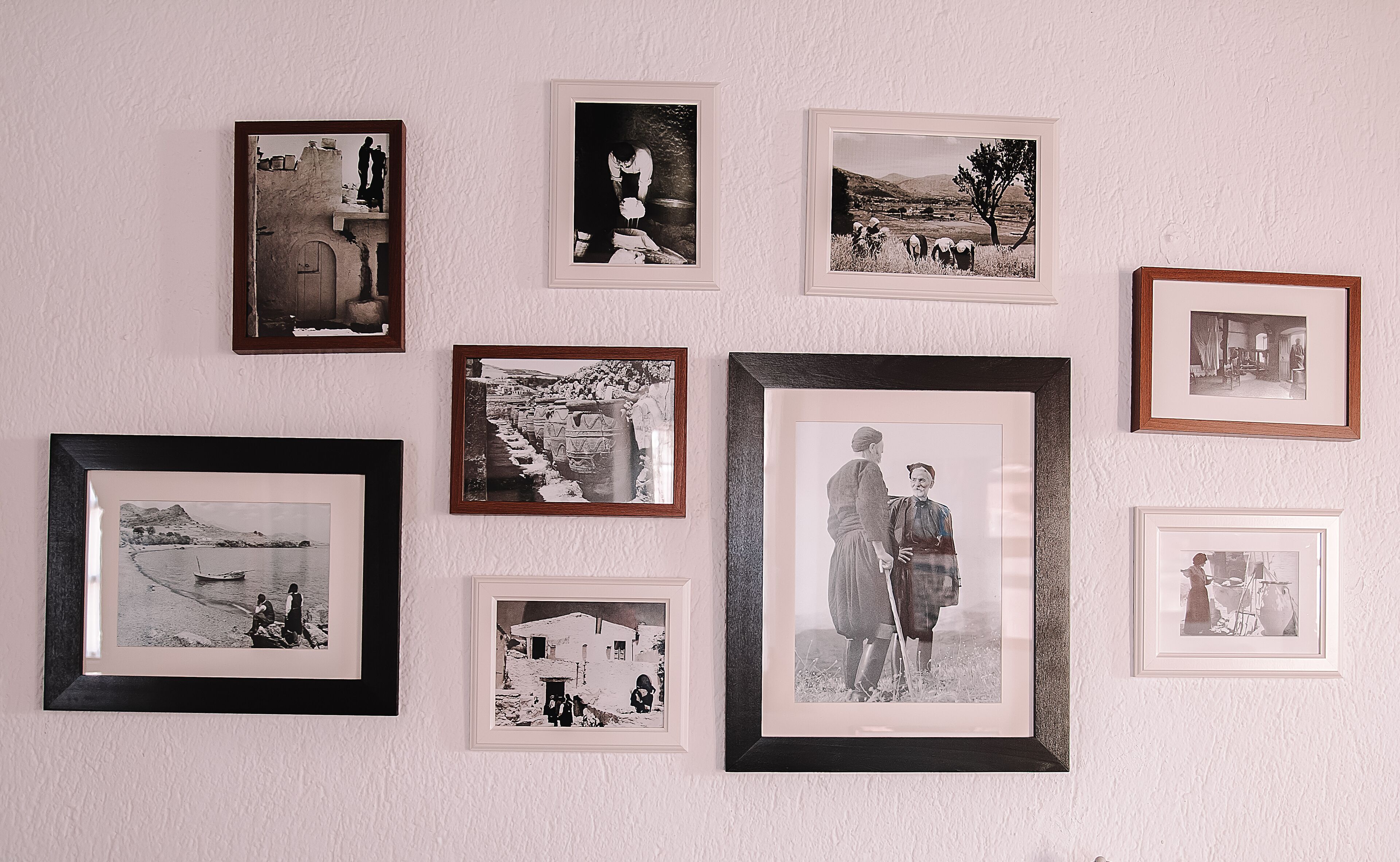 A wall with multiple framed black and white photographs of various scenes, including landscapes, people, and interiors.