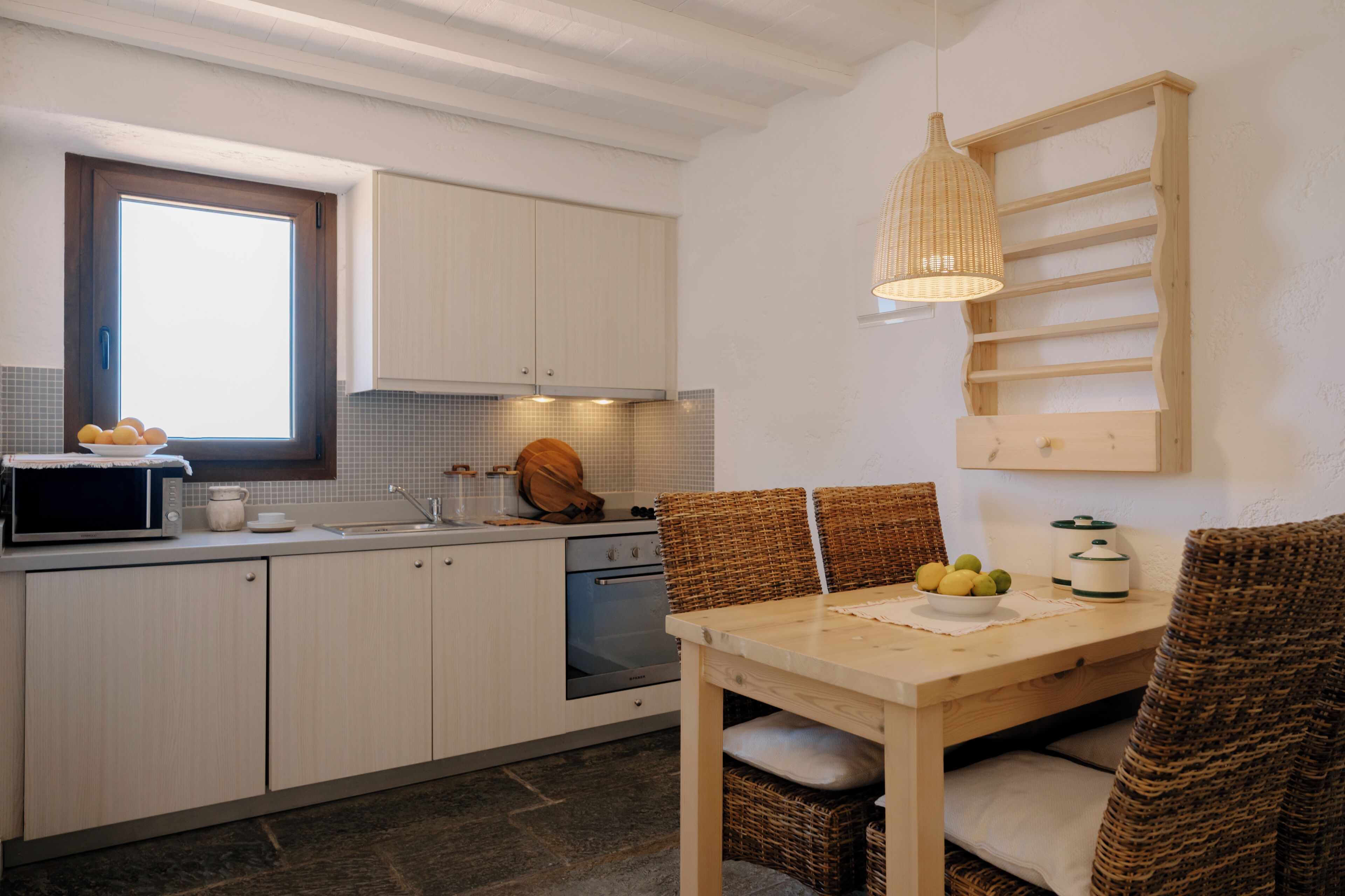 Una cocina con armarios blancos, microondas, fregadero y una mesa de madera con sillas.