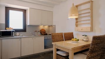 Una cocina con armarios blancos, microondas, fregadero y una mesa de madera con sillas.