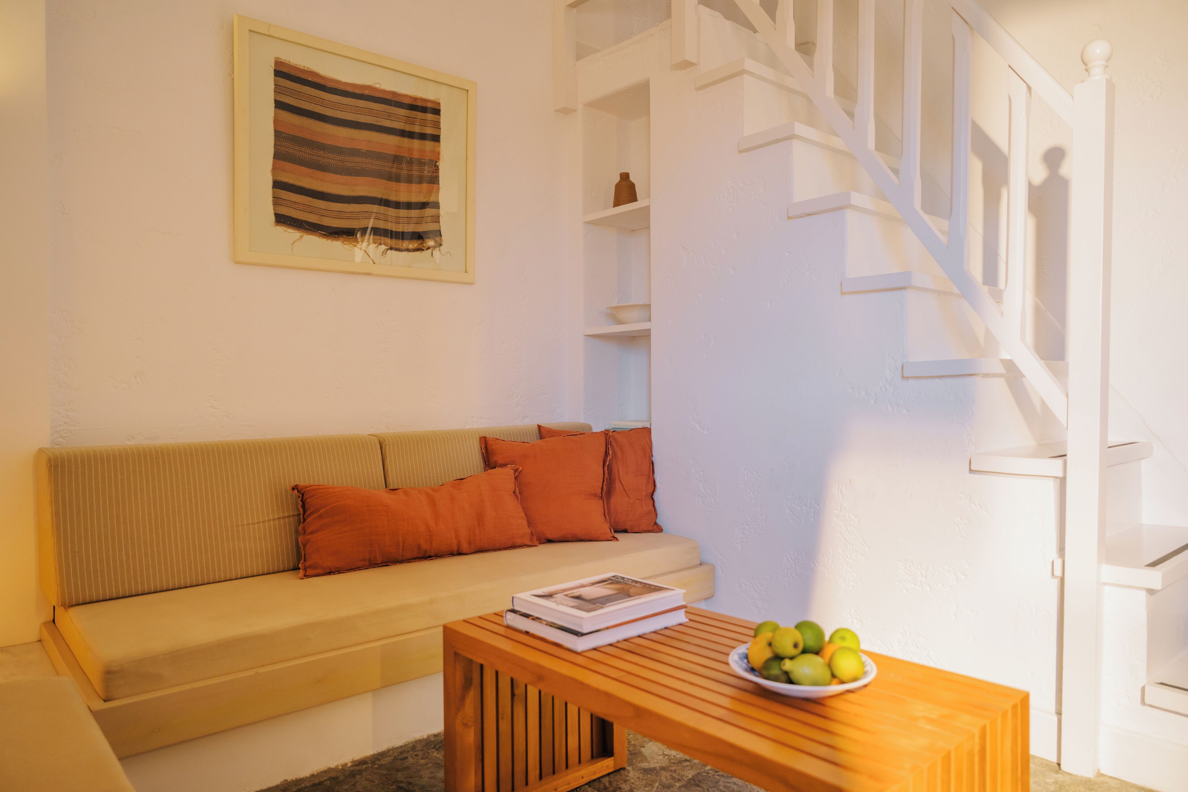 A living room with a sofa, a wooden coffee table with a bowl of fruit, a framed picture on the wall, and a staircase.