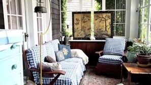 A cozy room with a checkered sofa and armchair, a wooden table, and a decorative screen with artwork. - Victorian Bed & Breakfast (Staten Island)