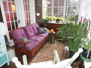 A cozy porch with a purple sofa, a small table, and various potted plants. - Victorian Bed & Breakfast (Staten Island)