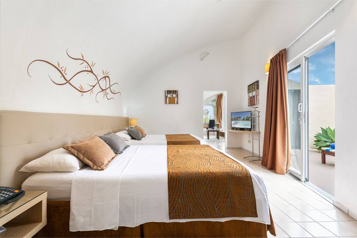 A hotel room with two beds, a desk, a TV, and a sliding glass door to the outside.