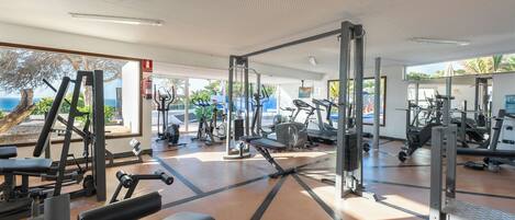 A gym with various exercise equipment, large windows, and a view of the outdoors.