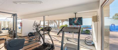 A gym with treadmills, stationary bikes, and a TV screen.