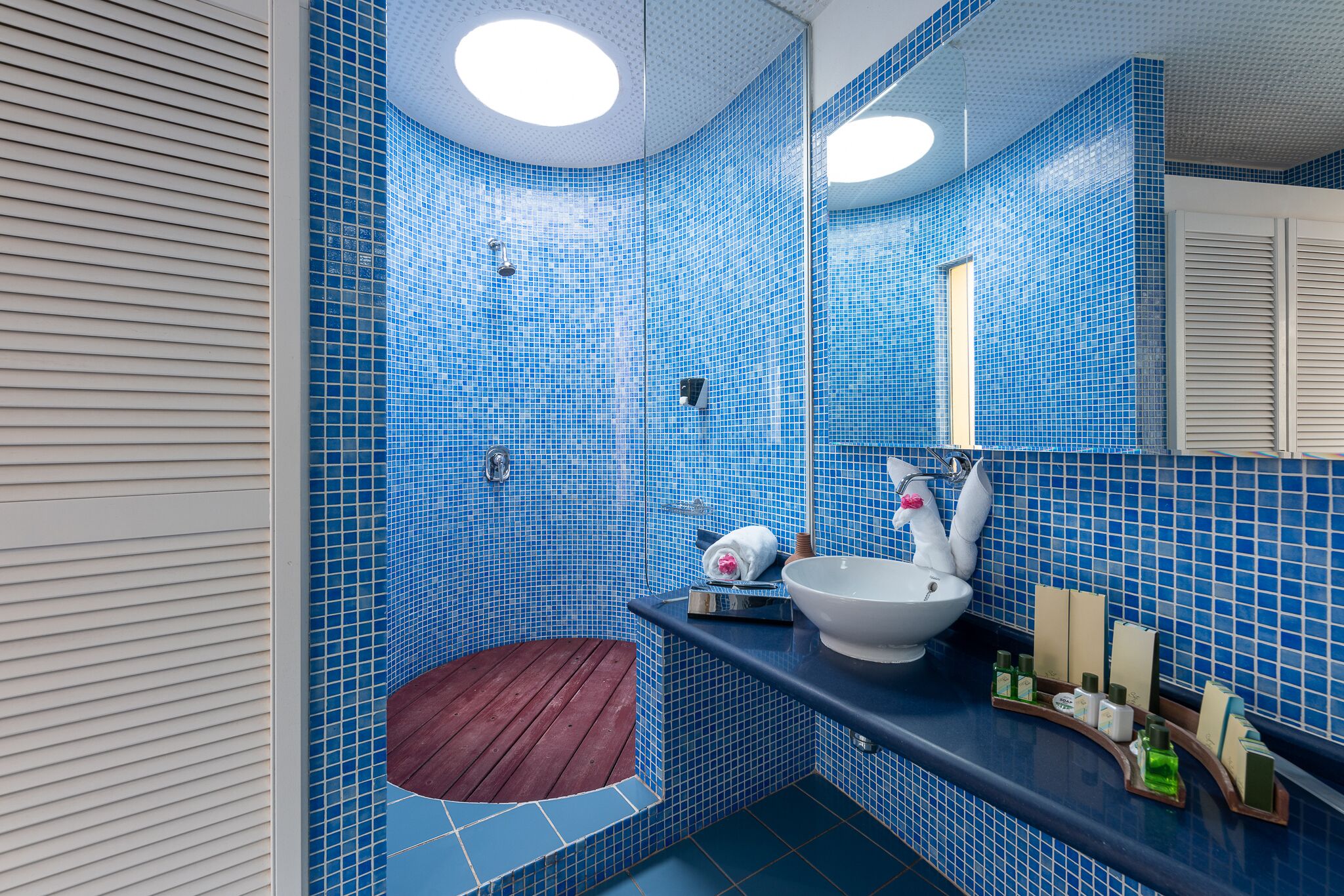 Een badkamer met blauwe betegelde wanden, een witte wastafel en een houten kruk.