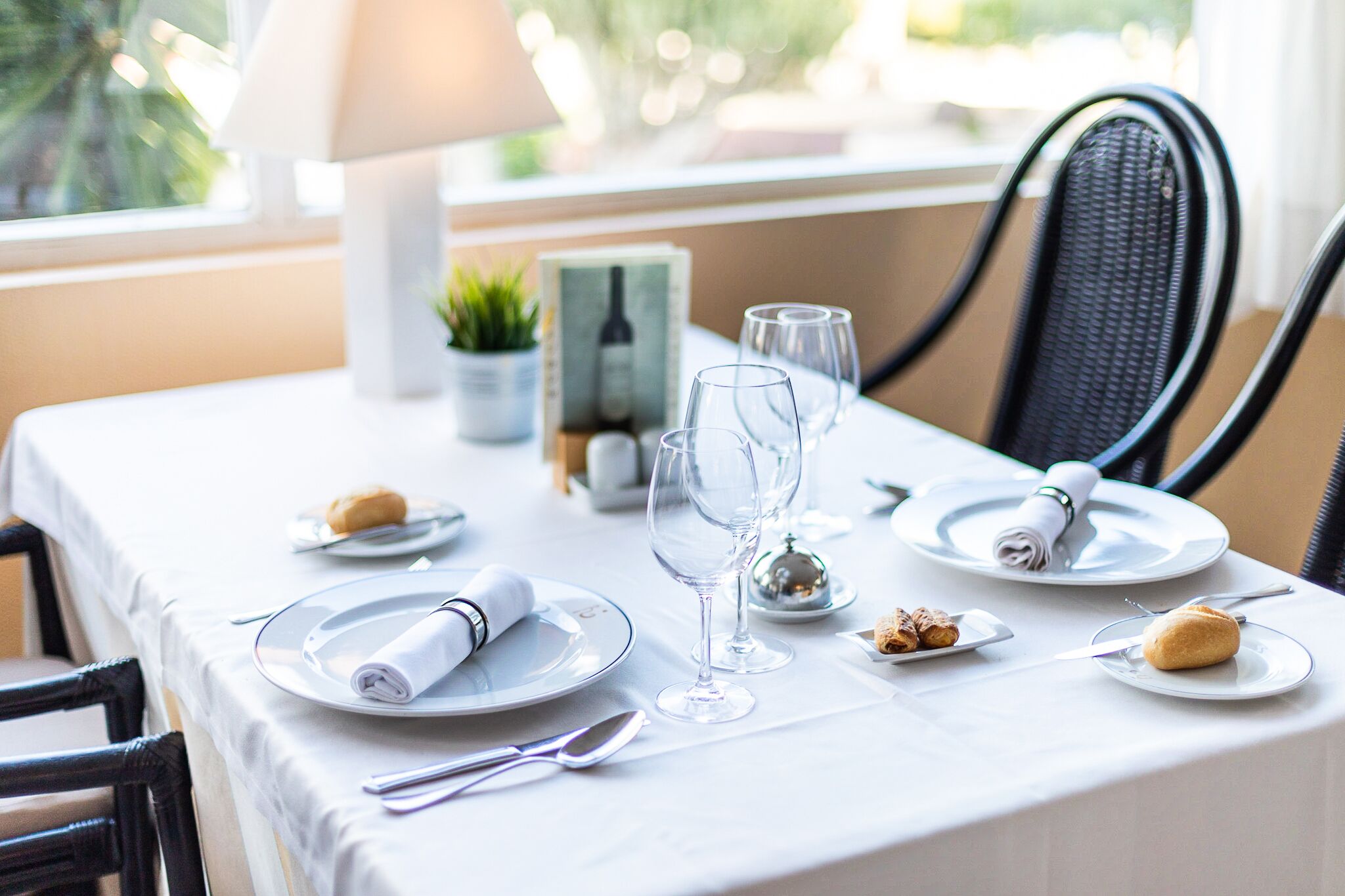 A dining table set with plates, glasses, and cutlery, a lamp, and a small potted plant.