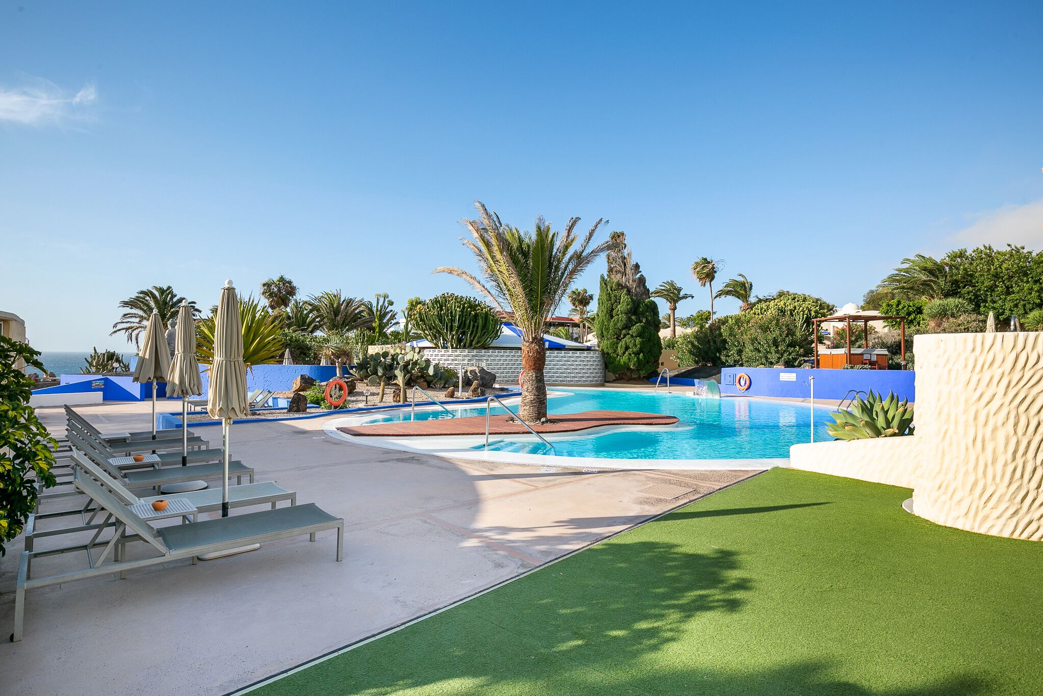 A pool area with lounge chairs, palm trees, and a clear blue sky.
