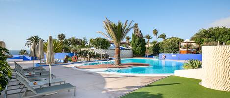 A pool area with lounge chairs, palm trees, and a clear blue sky.
