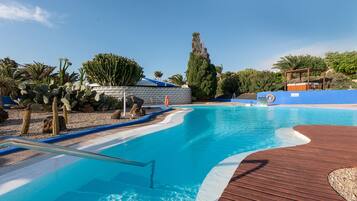 Una piscina con cubierta de madera, rodeada de cactus y palmeras.