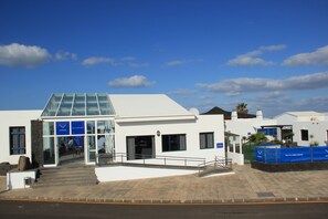 A modern building with a glass entrance, a staircase leading up to the entrance, and a blue sign with white text.