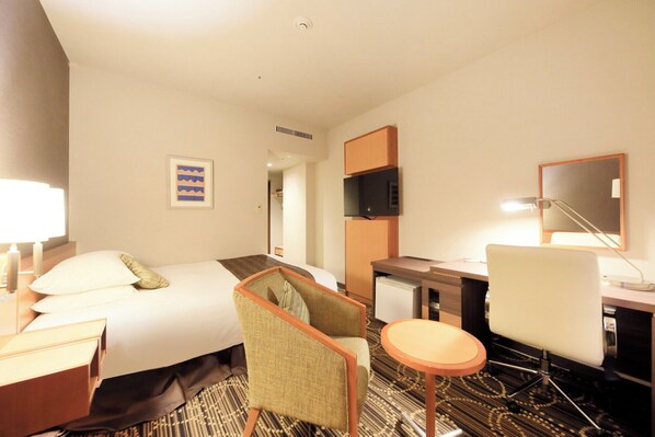 A hotel room with a bed, a desk, a chair, a TV, and a lamp.