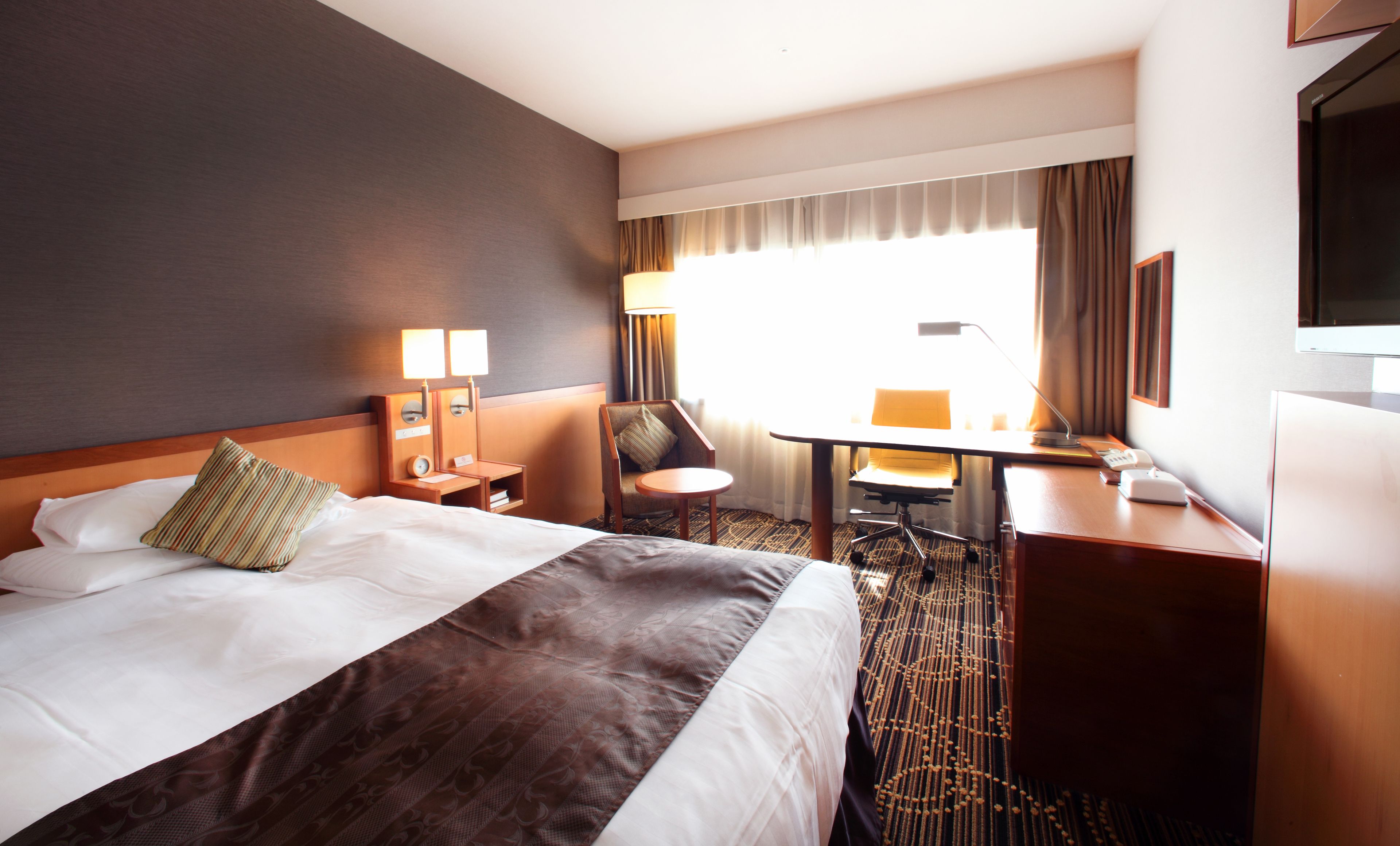 A hotel room with a large bed, a desk, a chair, and a TV.