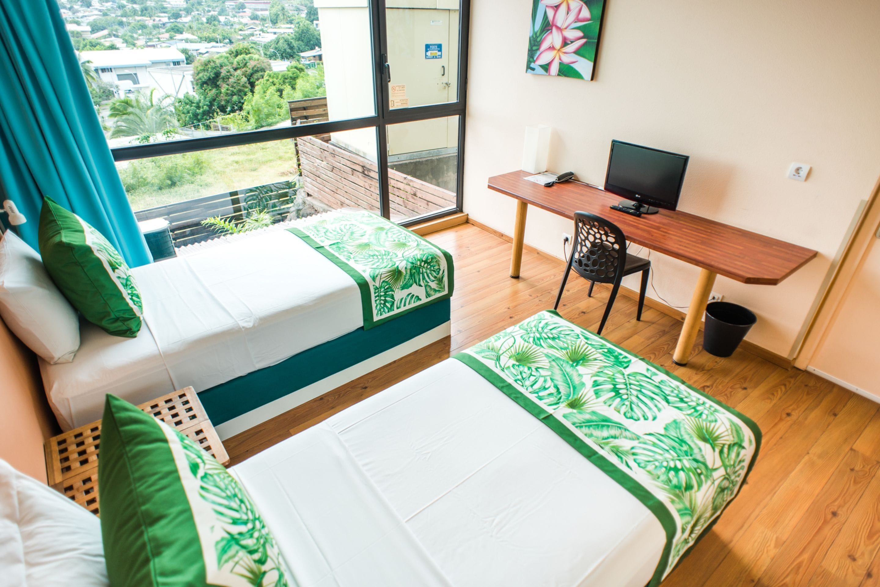 A room with two beds, a desk with a computer, and a window with a city view.
