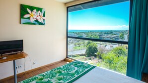 A bedroom with a large window, a bed, a TV on a stand, and a painting of flowers on the wall. - Tahiti Airport Motel (Faaa)