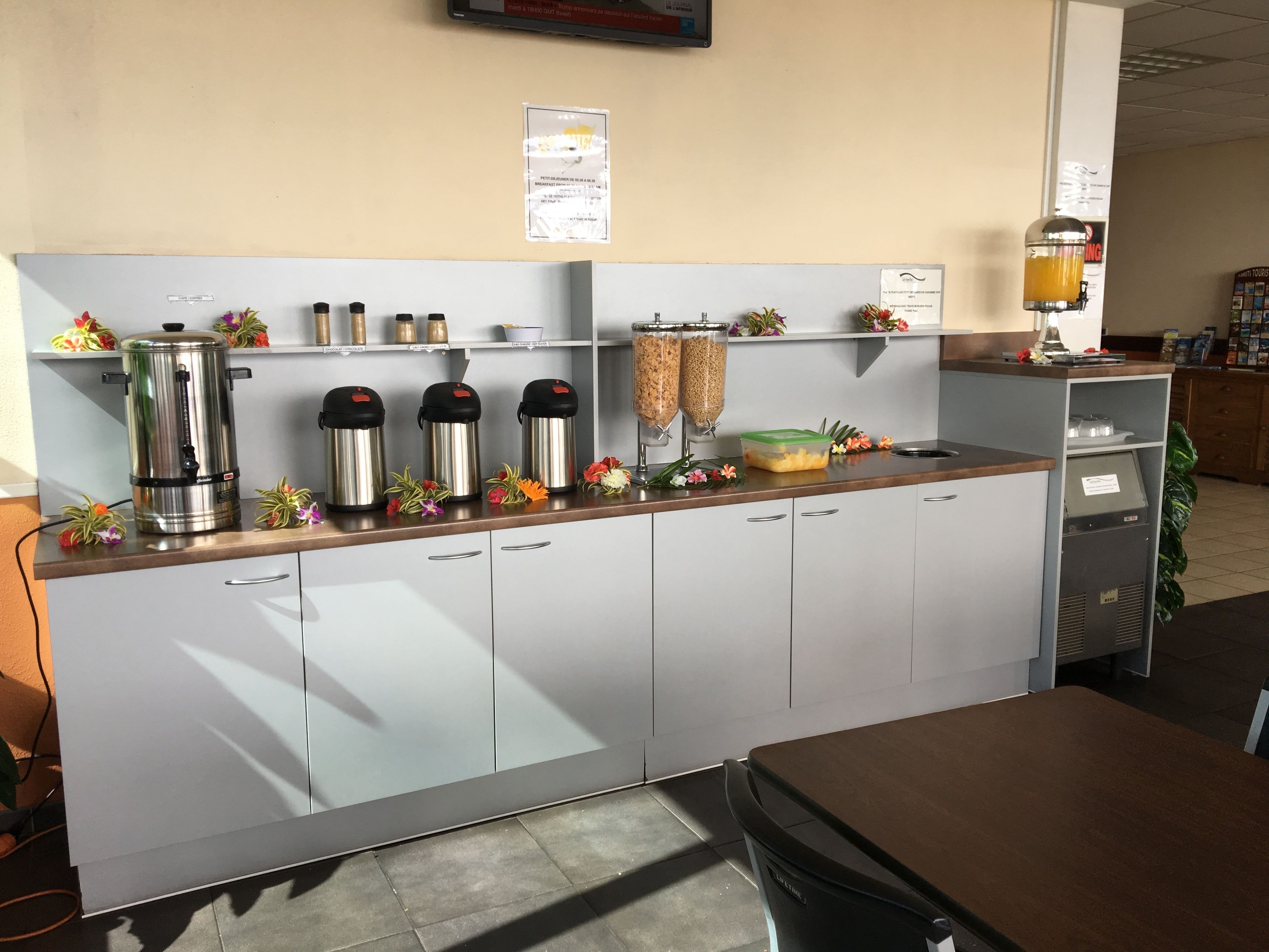 Una kitchenette con una macchina da caffè, due thermos e un piccolo distributore di succo, oltre a un frigorifero.