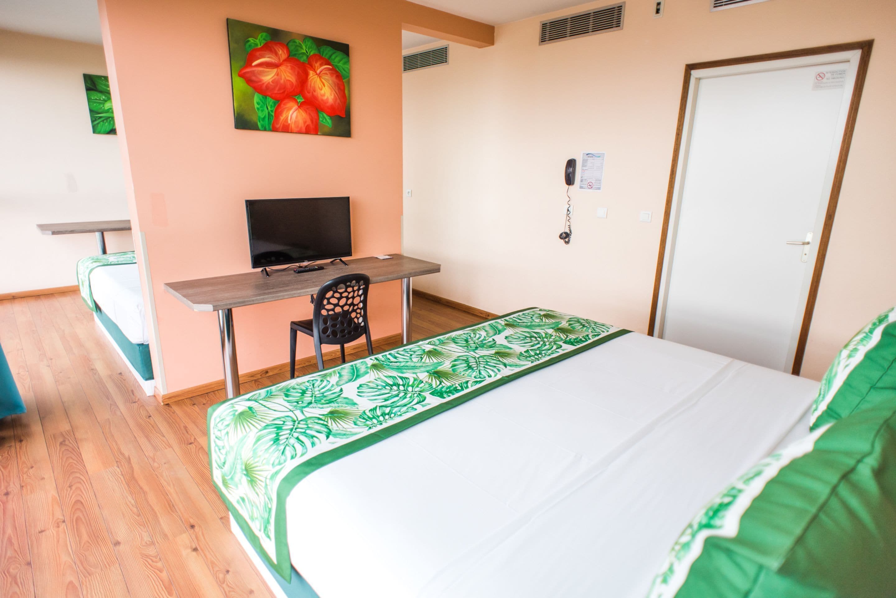 A hotel room with a bed, a desk with a computer, a chair, and a painting on the wall.