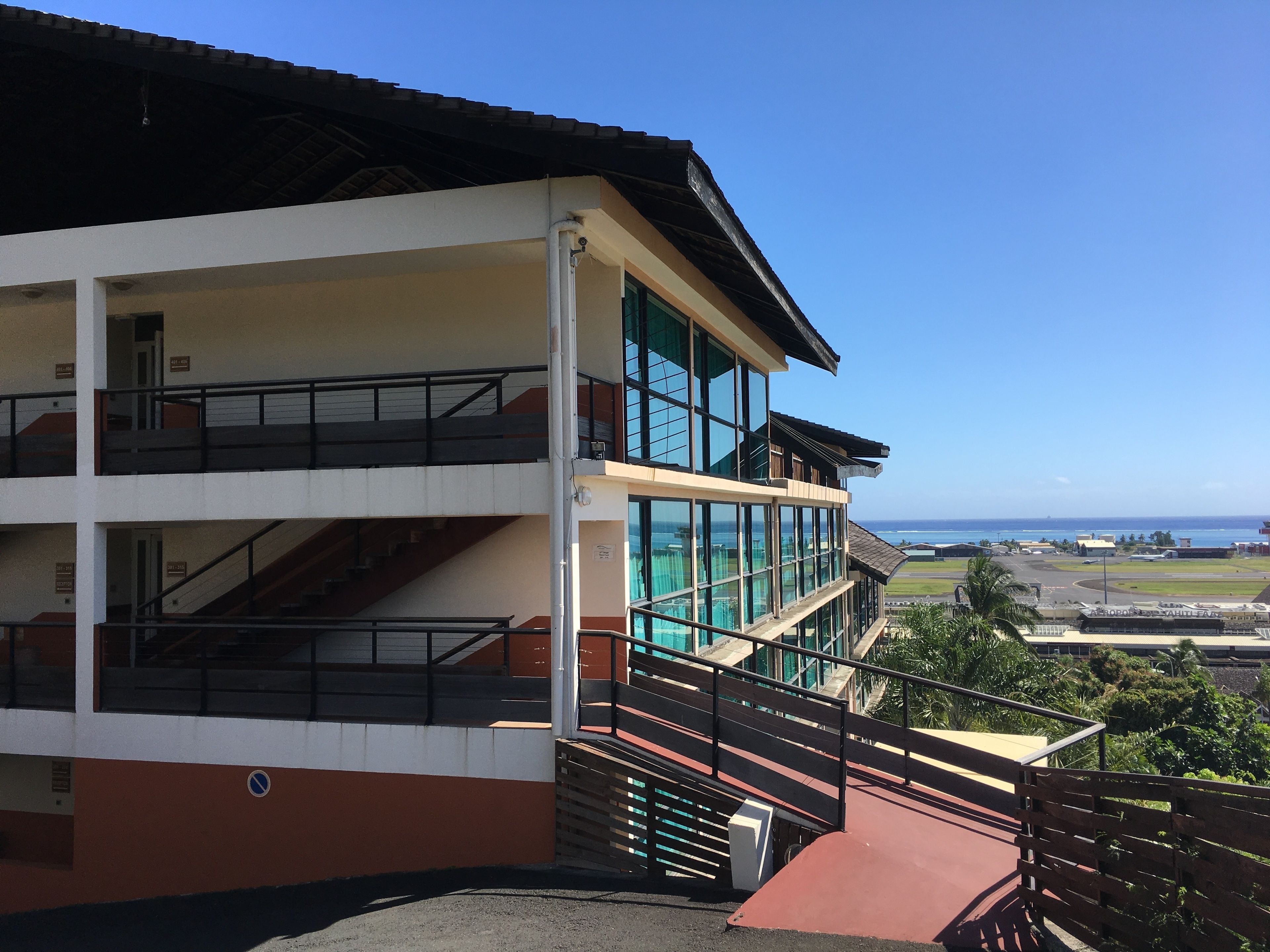A multi-story building with a red and white facade, large windows, and a view of the ocean.