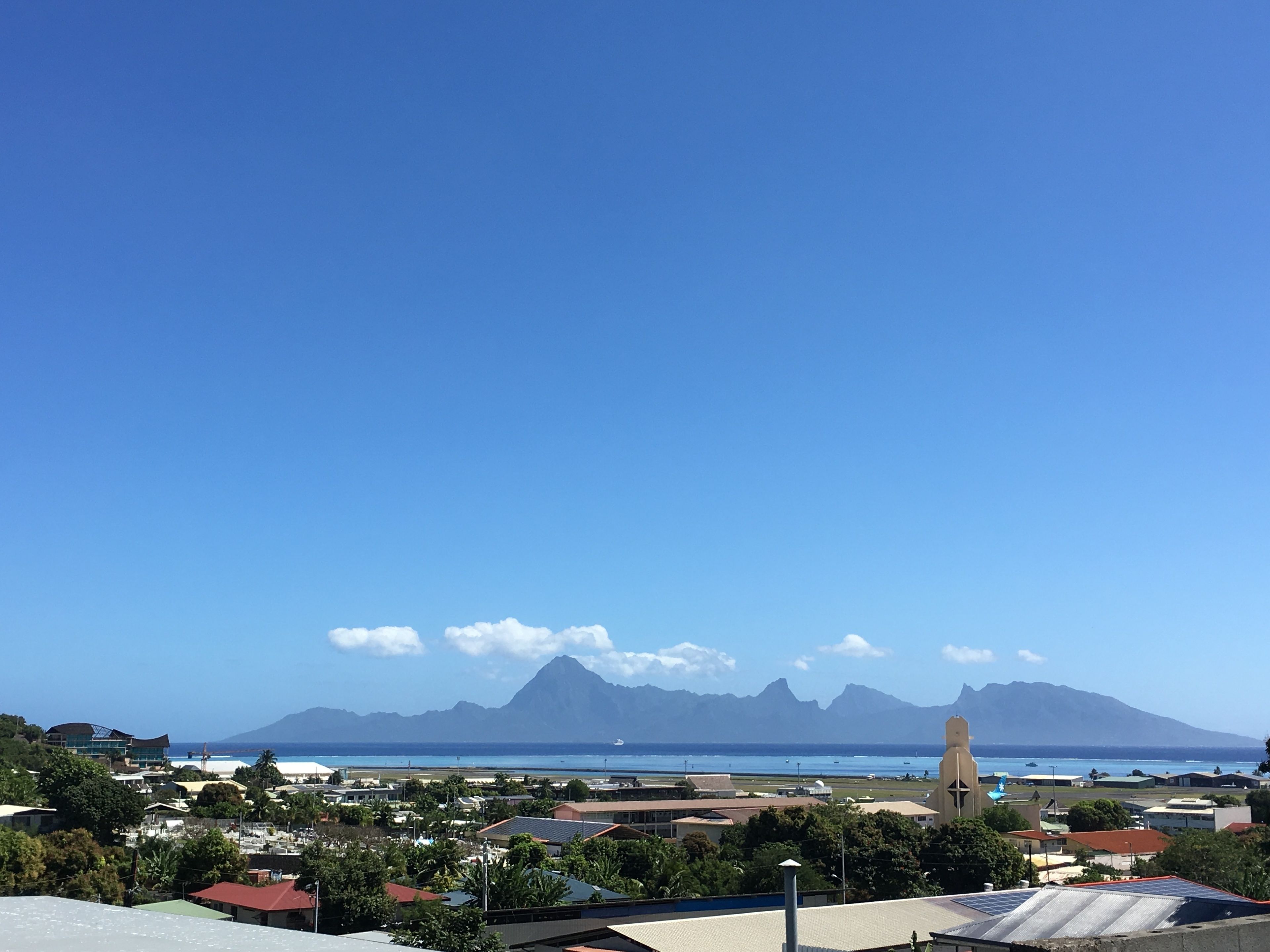 Una località costiera con una montagna imponente sullo sfondo, cieli sereni e vista sull'oceano.