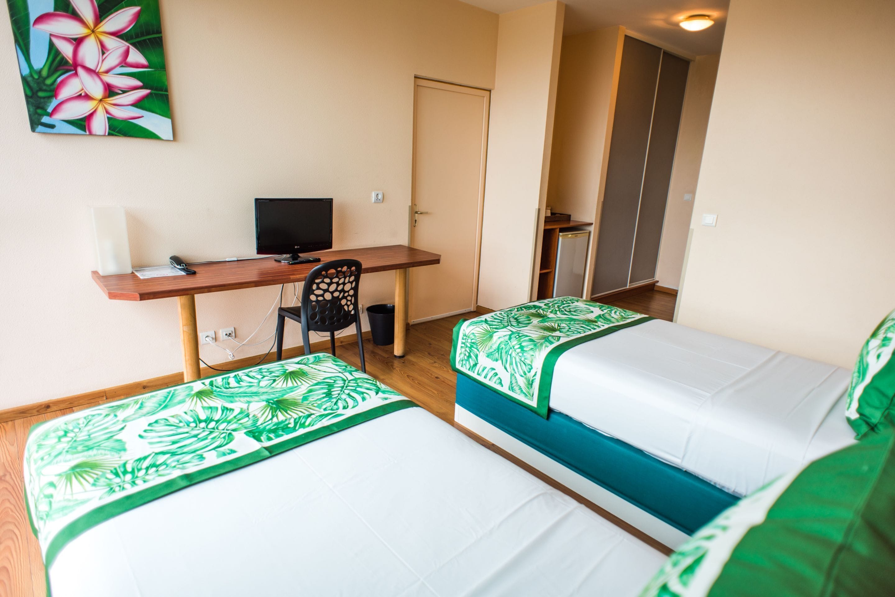 A hotel room with two beds, a desk with a computer, a chair, and a door leading to a closet.