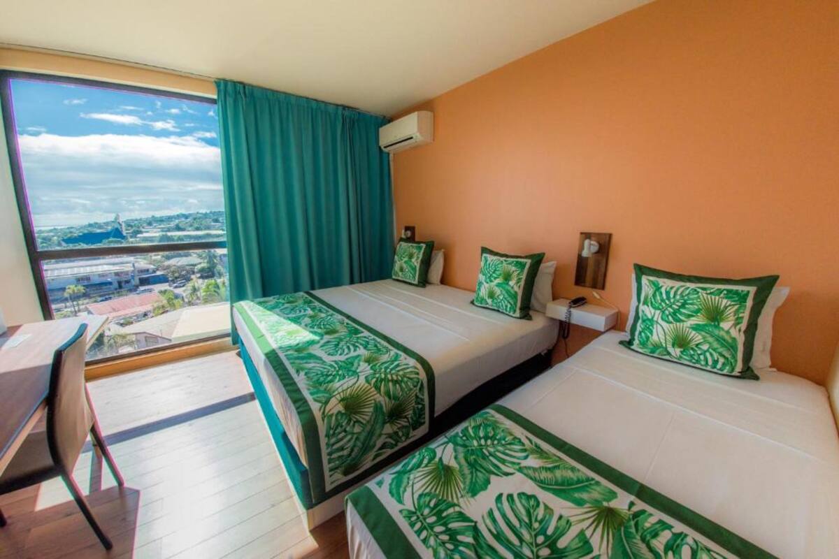 A hotel room with two beds, a desk, and a large window with a view of a cityscape.