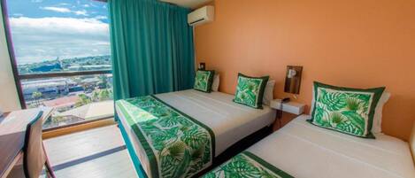 Une chambre d’hôtel avec deux lits, un bureau et une grande fenêtre donnant sur un paysage urbain.