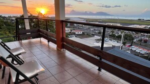 A balcony with a view of a sunset over a coastal area, including mountains and a marina. - Tahiti Airport Motel (Faaa)