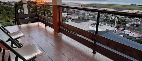 A balcony with a view of a sunset over a coastal area, including mountains and a marina.
