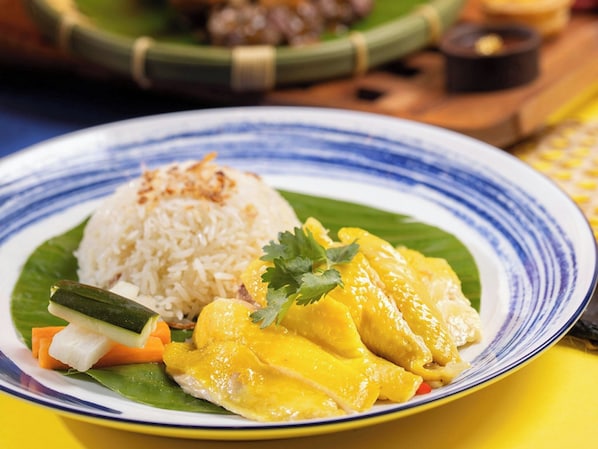 Ein Teller mit Reis, Gemüse und einem gelben Gericht, möglicherweise Curry, auf einem Bananenblatt.