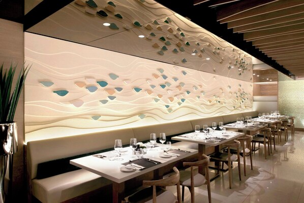 A modern restaurant with a long counter, cushioned seating, and a decorative wall.