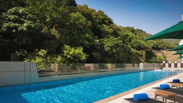 A swimming pool with lounge chairs and umbrellas, surrounded by lush greenery.