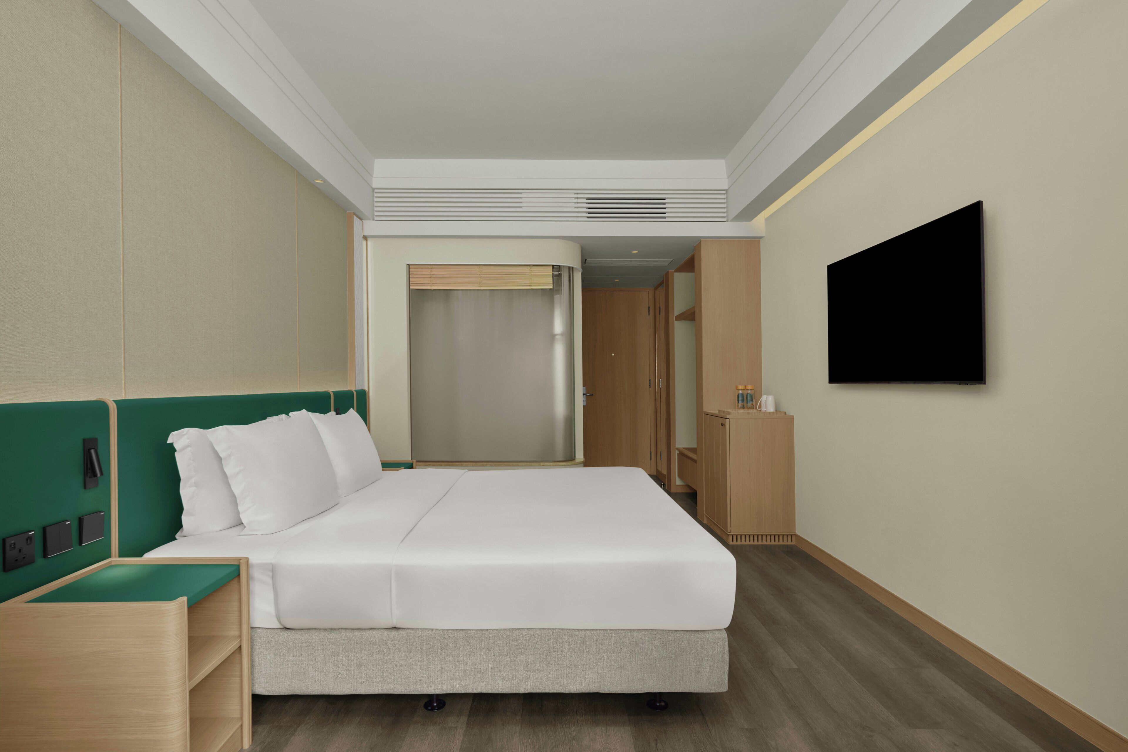 Une chambre d’hôtel avec un lit, un téléviseur fixé au mur, une tête de lit en bois et un placard.
