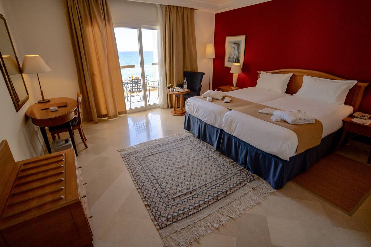 Habitación de hotel con cama, escritorio, silla, mesita y vistas al mar a través de la ventana.