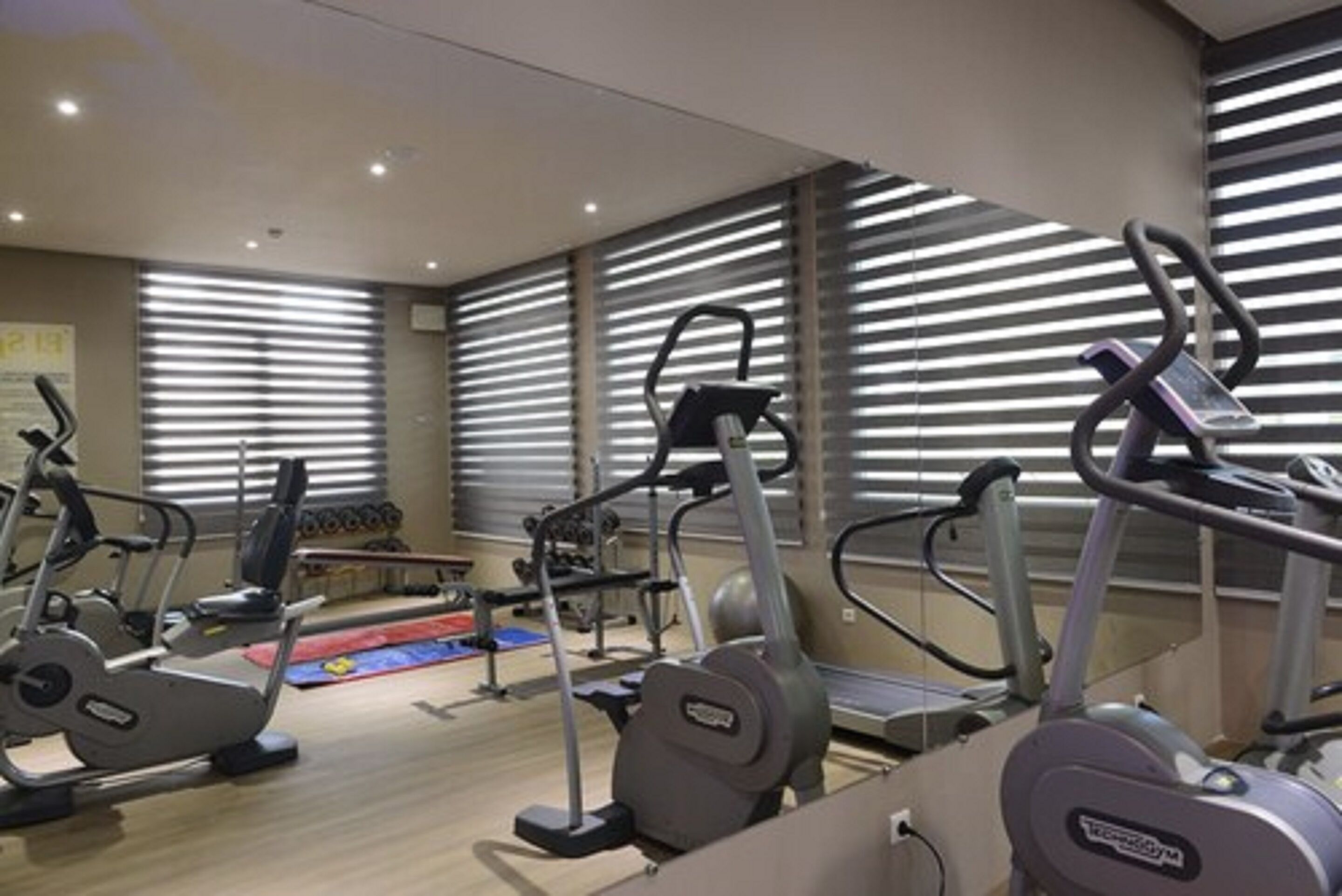 Un gimnasio con diferentes máquinas de cardio, una banca y una zona pequeña para estirar.
