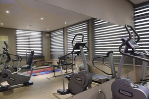 Un gimnasio con diferentes máquinas de cardio, una banca y una zona pequeña para estirar.