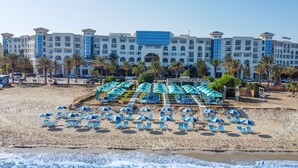 A beachfront hotel with multiple blue umbrellas and lounge chairs, a pool area, and a large building with a modern design. - Vincci Saphir Palace & Spa (Hammamet)
