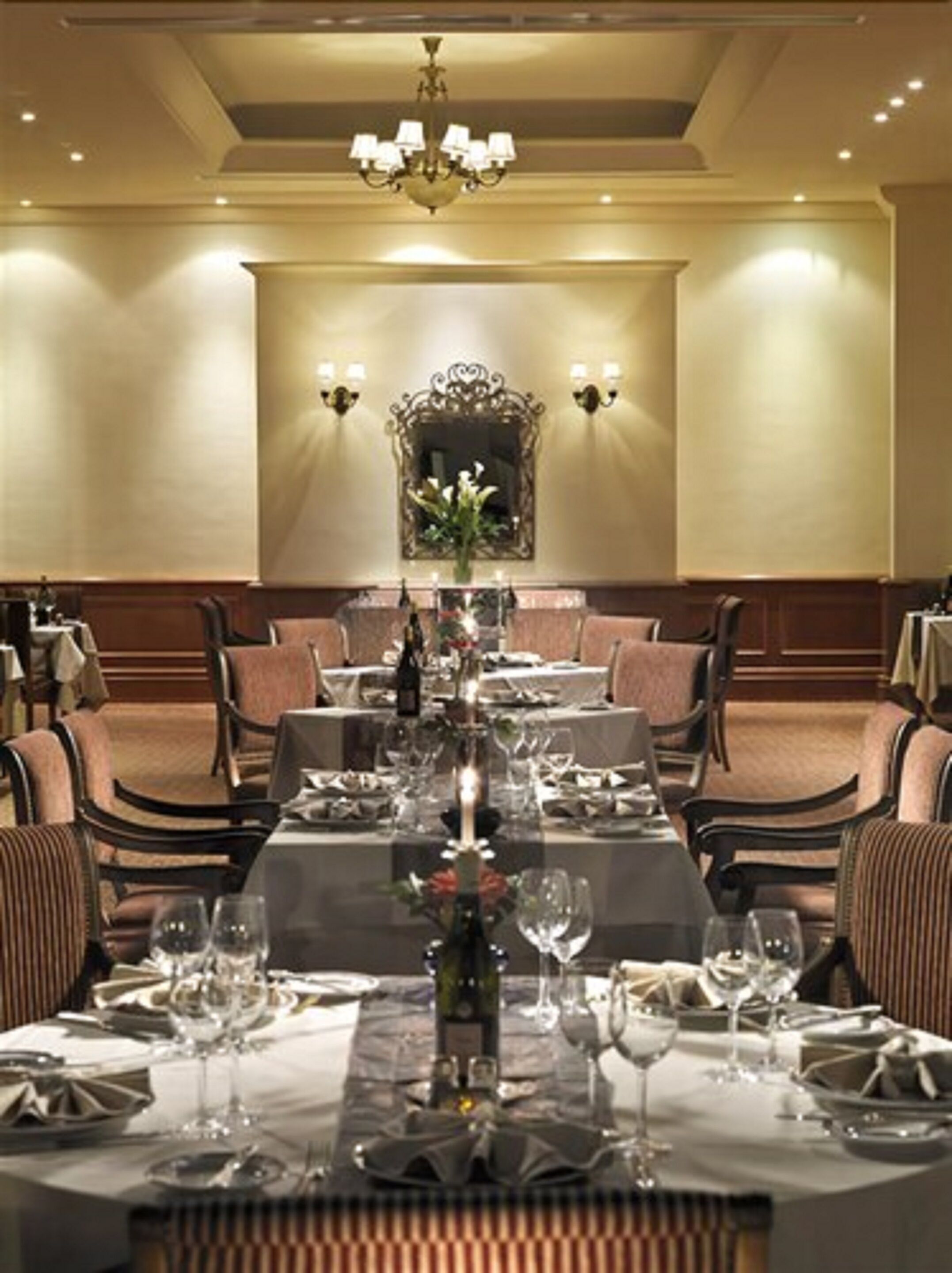 Un comedor elegante con una larga mesa dispuesta para una comida, flanqueada por sillas tapizadas, un candelabro y apliques de pared.