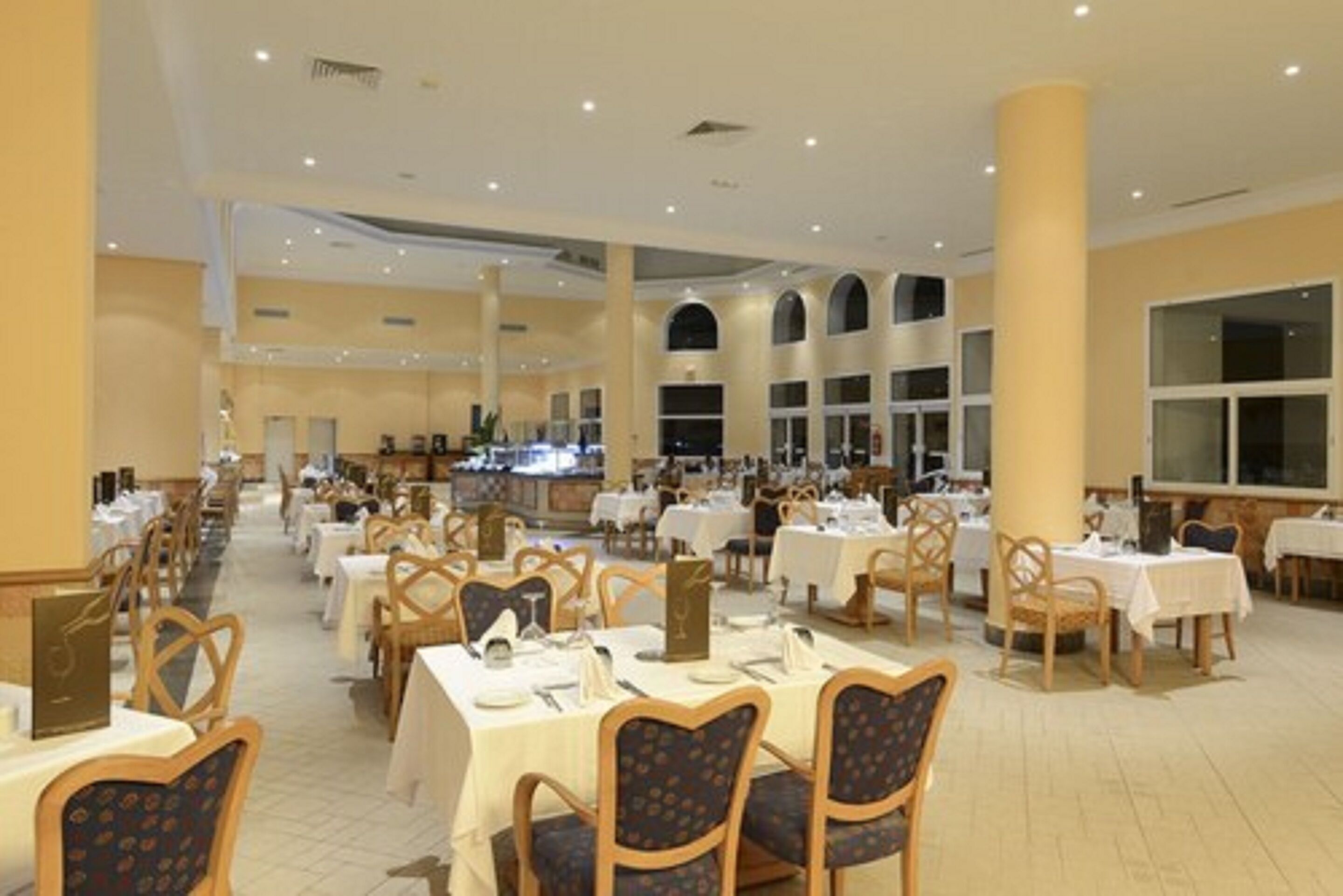 A spacious dining area with multiple tables and chairs, large windows, and a high ceiling.