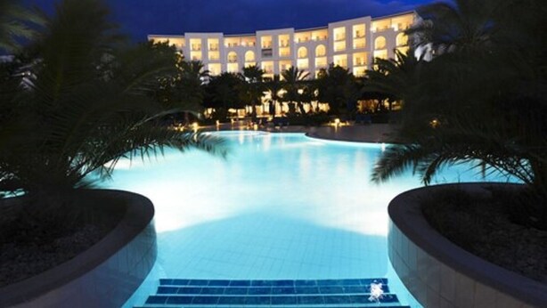 A hotel with a large swimming pool surrounded by palm trees and a well-lit building facade. - Vincci Saphir Palace & Spa (Hammamet)