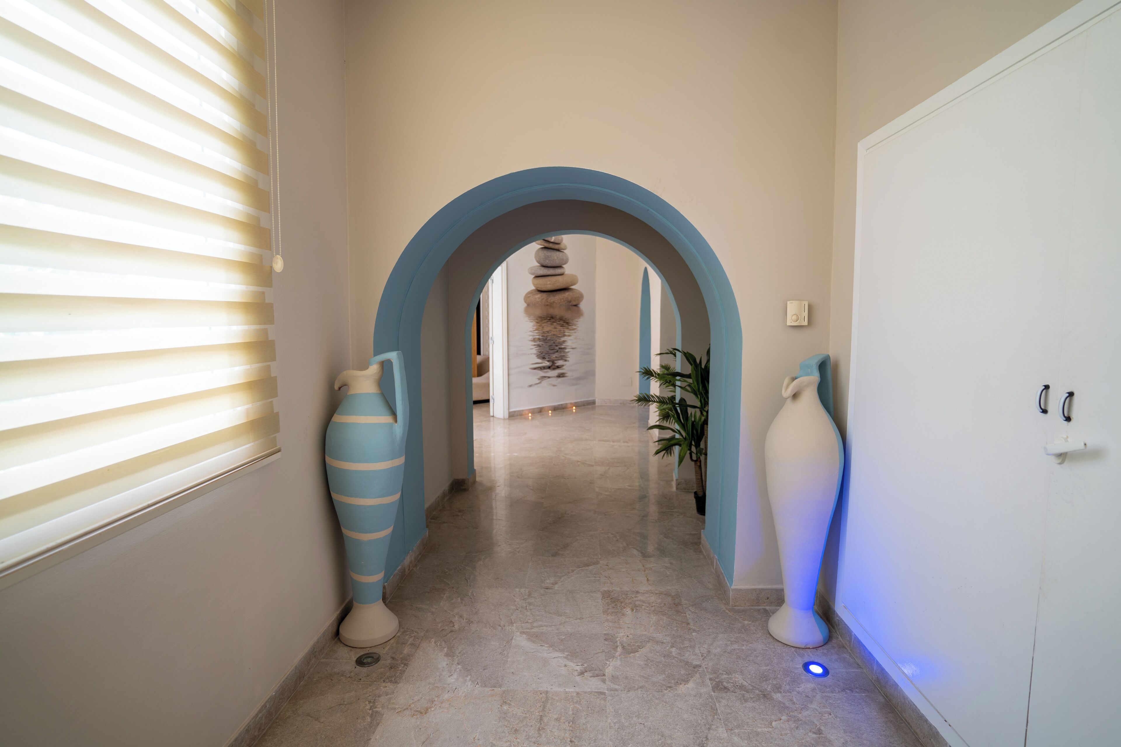 Un pasillo con un arco azul, una pila de piedras y grandes jarrones.