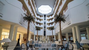 A spacious lobby with a central seating area, multiple floors, and a large skylight. - Vincci Saphir Palace & Spa (Hammamet)