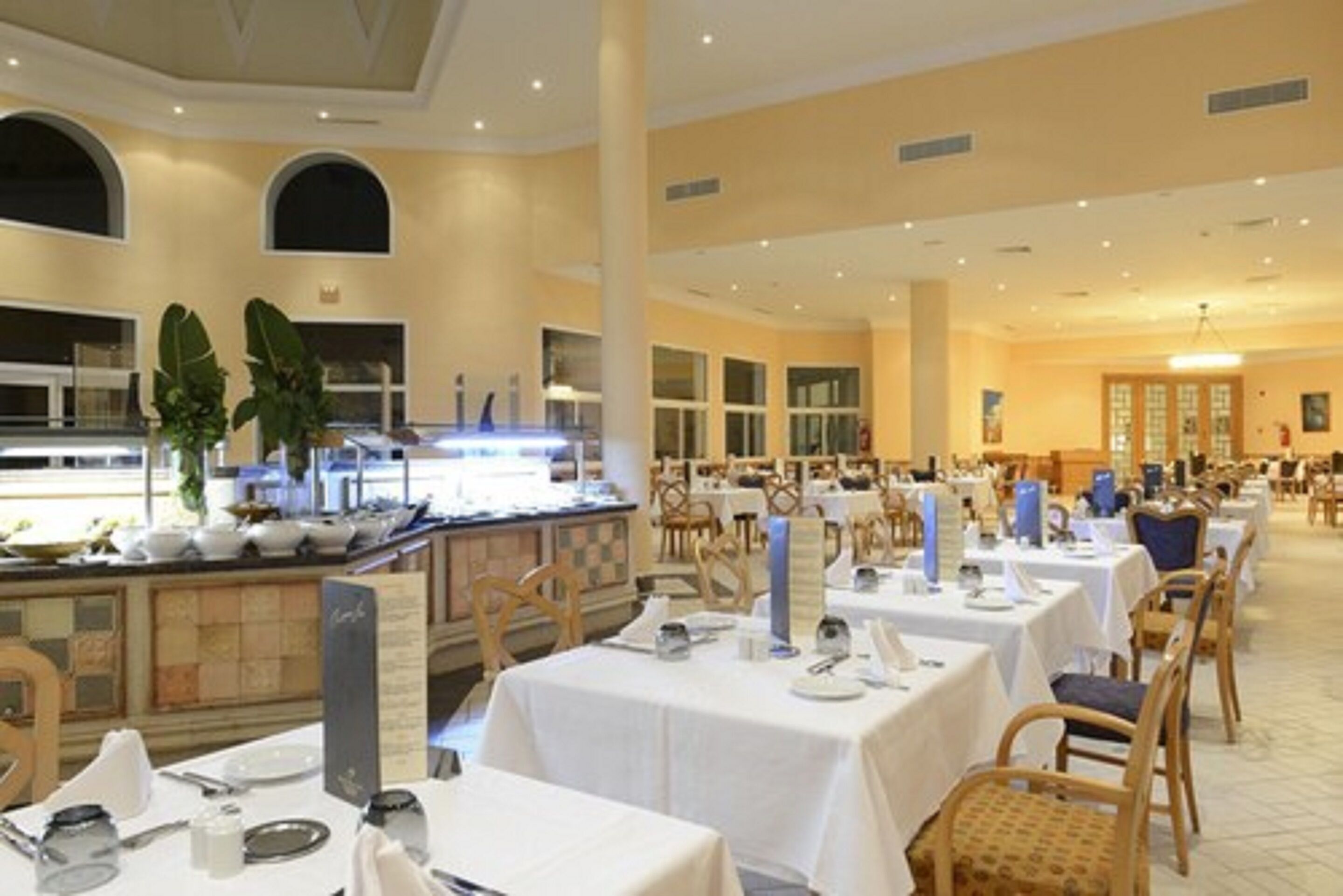 Un amplio comedor con varias mesas y sillas, una barra de buffet y un techo alto con iluminación empotrada.