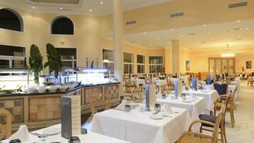 Un amplio comedor con varias mesas y sillas, una barra de buffet y un techo alto con iluminación empotrada.