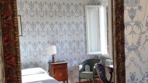 Quarto com um espelho grande, uma cama, uma mesa de cabeceira, uma cadeira e um radiador.