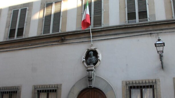 Fachada de edifício com estátua, bandeira e poste de luz.