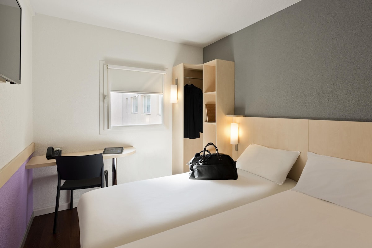 Een hotelkamer met een bed, nachtkastje, stoel, bureau en een kledingkast.