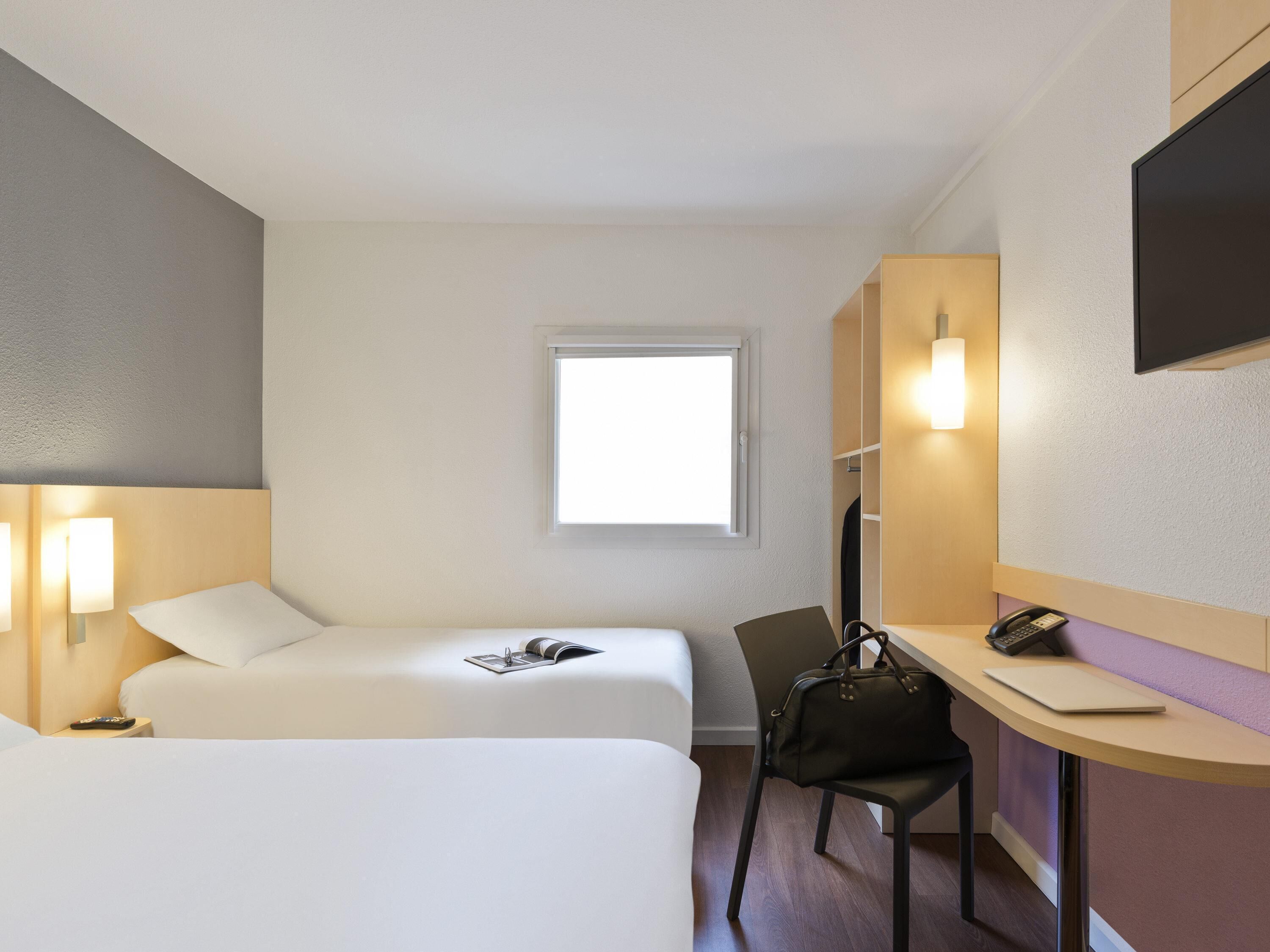 Une chambre d’hôtel avec deux lits, un bureau avec une chaise, un téléphone et une fenêtre.