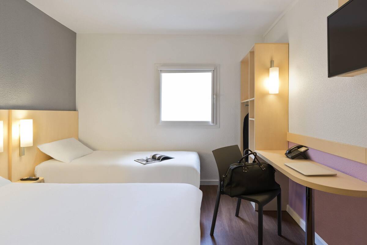 Een hotelkamer met twee bedden, een bureau met stoel, een telefoon en een raam.