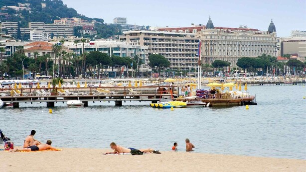 A coastal cityscape with a beach, a pier with boats, and a large building with the name 'Carlton' visible. - ibis budget Cannes centre ville (Cannes)
